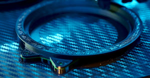 A close-up of a carbon fiber 3D printer producing a ring-shaped part under a bright blue light.