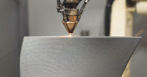 A close-up of a 3D printer nozzle. The printer utilizes a high-temperature printing process to create a custom metal product.