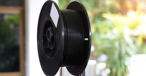 A large spool of carbon fiber filament materials mounted on top of a 3D printer to feed printing processes.