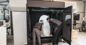 Two manufacturing technicians lifting a large prototype out of their commercial-grade 3D printing system.